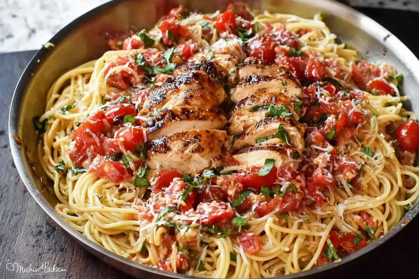 A skillet of bruschetta chicken pasta with sliced chicken breast, fresh diced tomatoes, basil, and parmesan.
