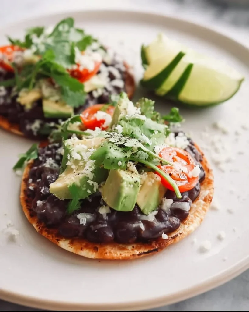 Black bean tostadas topped with fresh vegetables and salsa on a wooden plate